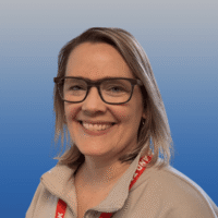 Photo of a woman with dark blonde shoulder length hair smiling. She is wearing glasses and a beige collared shirt.
