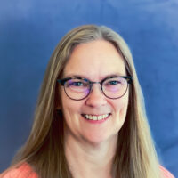 Margie Roe is an Educational Assistant at Listen and Talk's blended classroom preschool program for children who are deaf and hard of hearing. She is a white woman wearing glasses and a pink shirt. She has blonde hair.