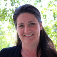 Photo of a woman with long dark hair pulled back from her face. She has dark brown eyes and is smiling