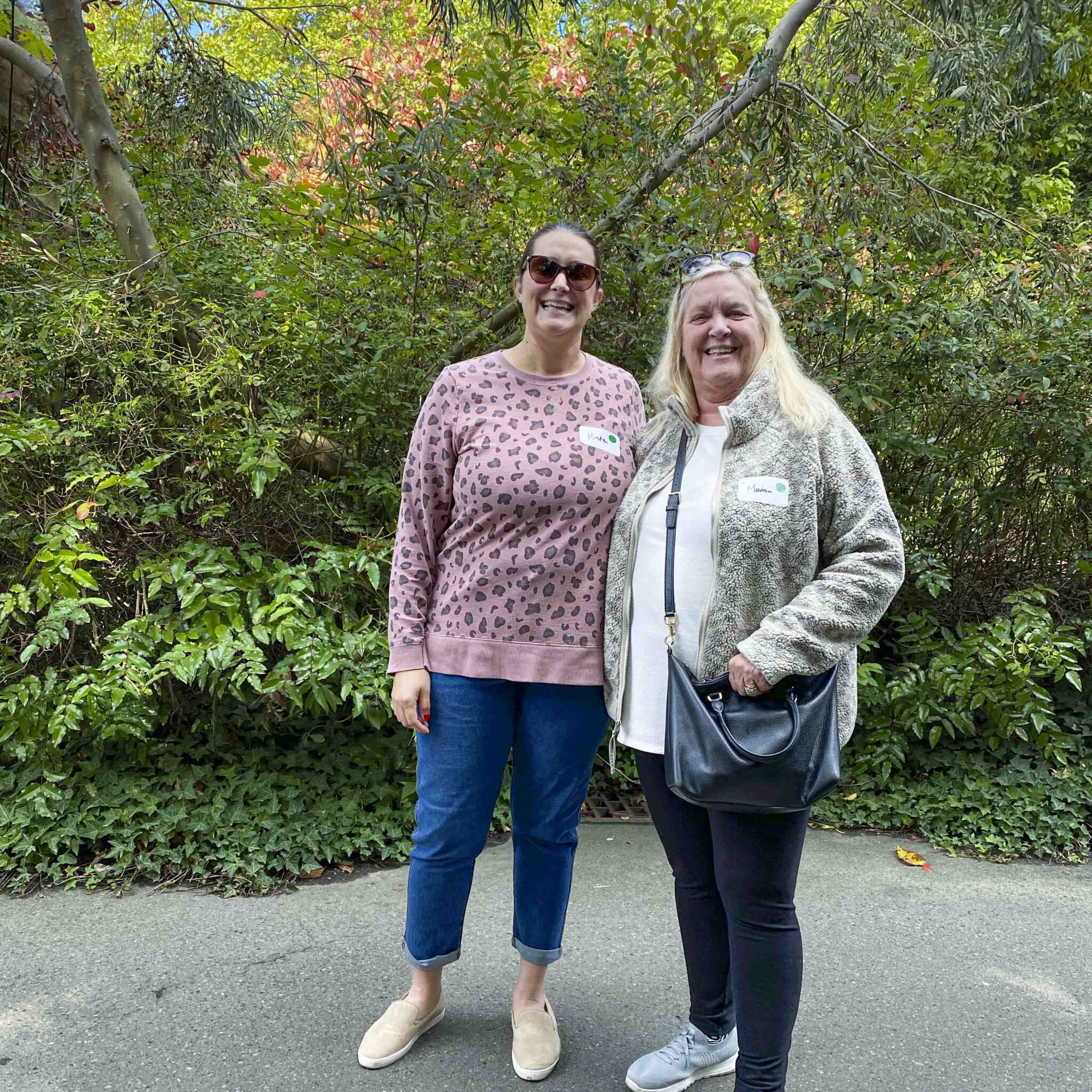 Two adult women walk together on a paved pathway in a wooded area at the Zoo.