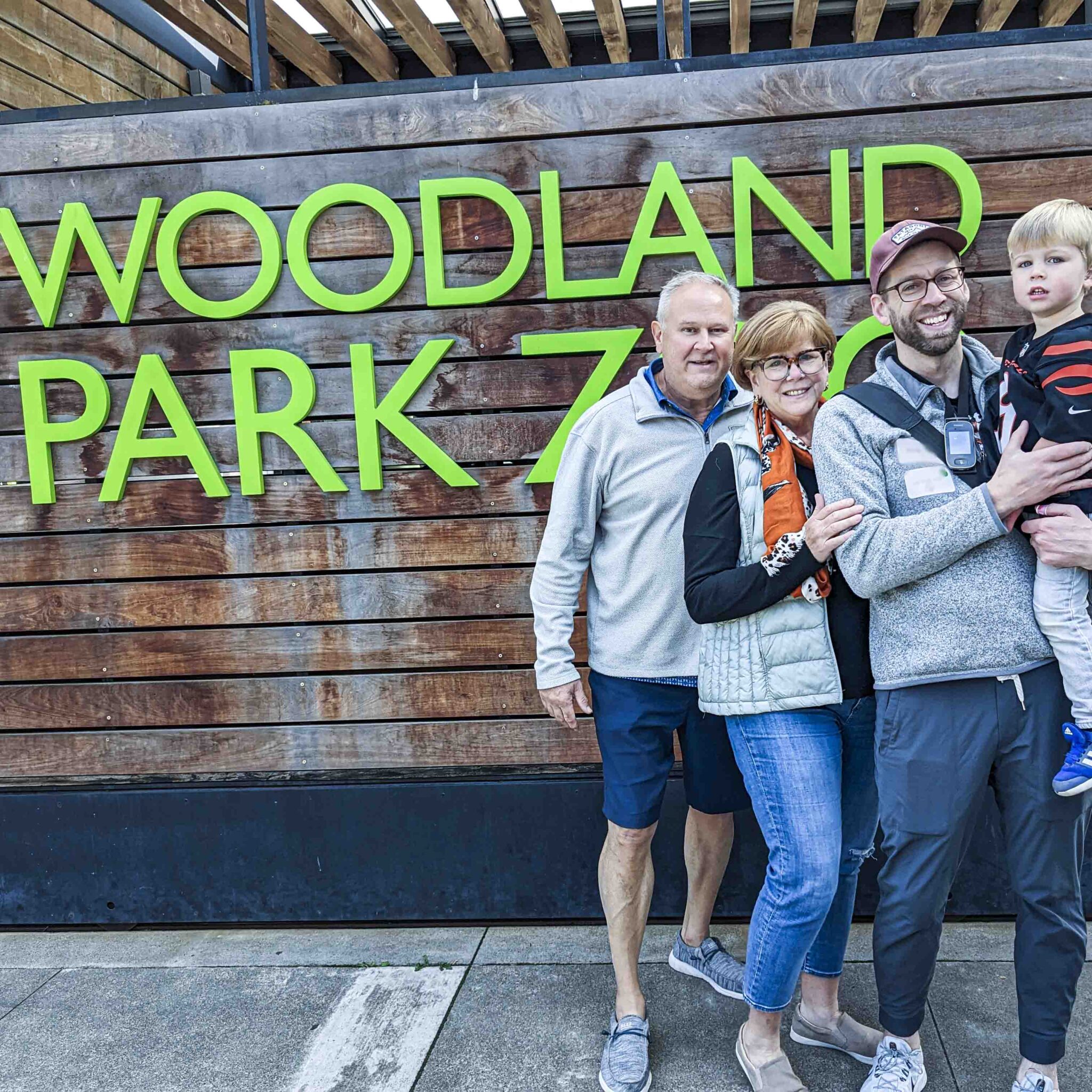 A family poses for a photo in front of Woodland Park Zoo sign.