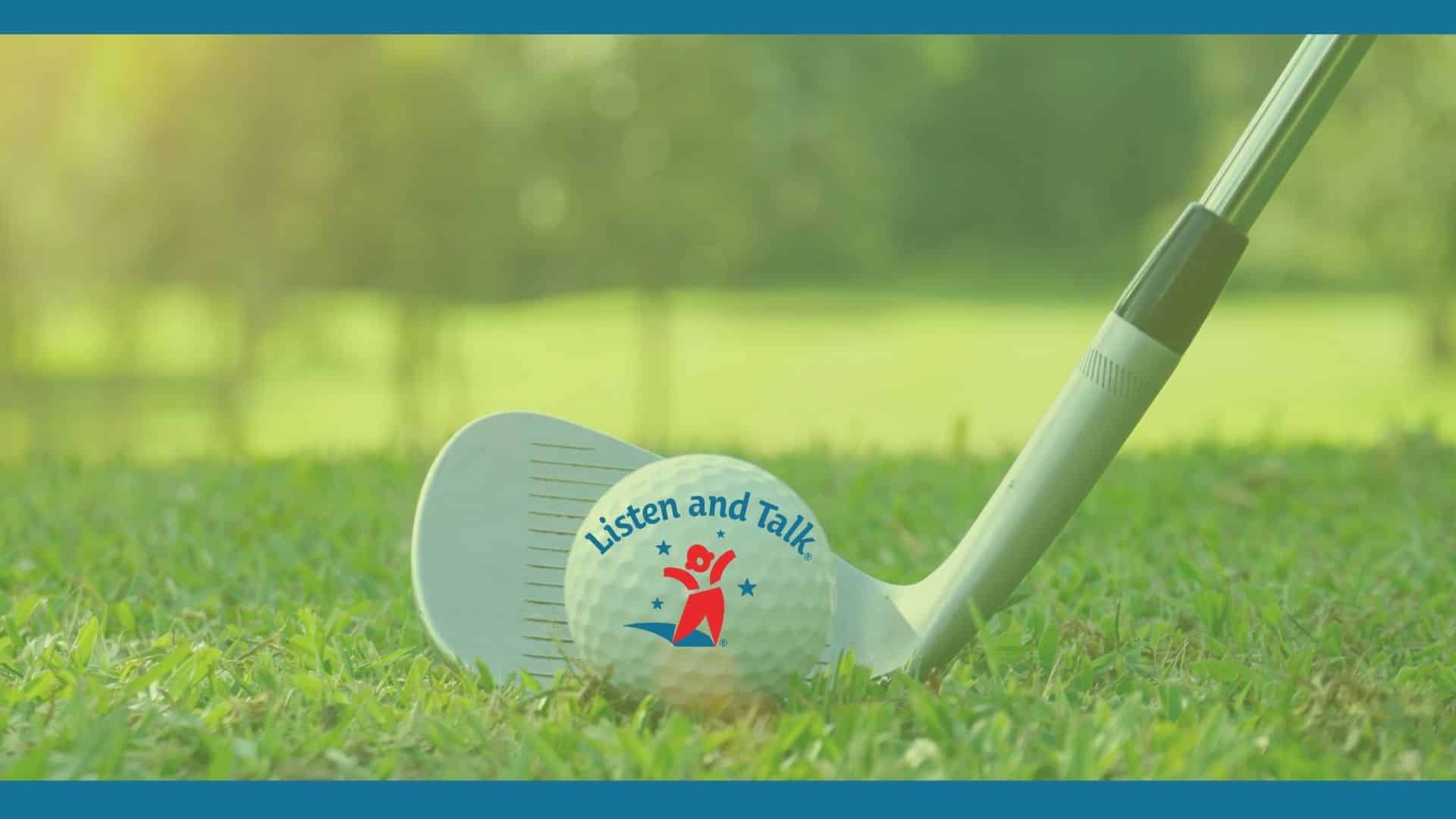 Golf club sitting on green grass lined up with a golf ball that has a listen and talk logo of a child with outstretched arms in red