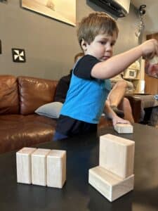 Child with hearing aid wearing light blue LENA vest playing with wooden blocks