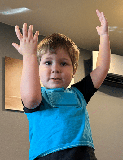 Young boy with hands up above his head wearing a light blue LENA vest