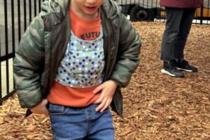 Preschool aged boy wears blue LENA vest while playing on the playground at Listen and Talk playground