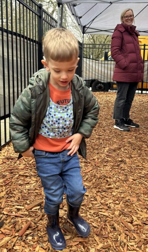 Preschool aged boy wears blue LENA vest while playing on the playground at Listen and Talk playground