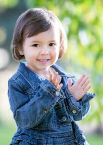 Photo of young girl with brown hair and brown eyes wearing a blue denim dress.