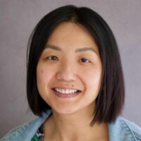 Photo of a woman with straight black shoulder length hair.She is smiling. She has brown eyes and medium toned skin. She is wearing a jean jacket and a flowered top.