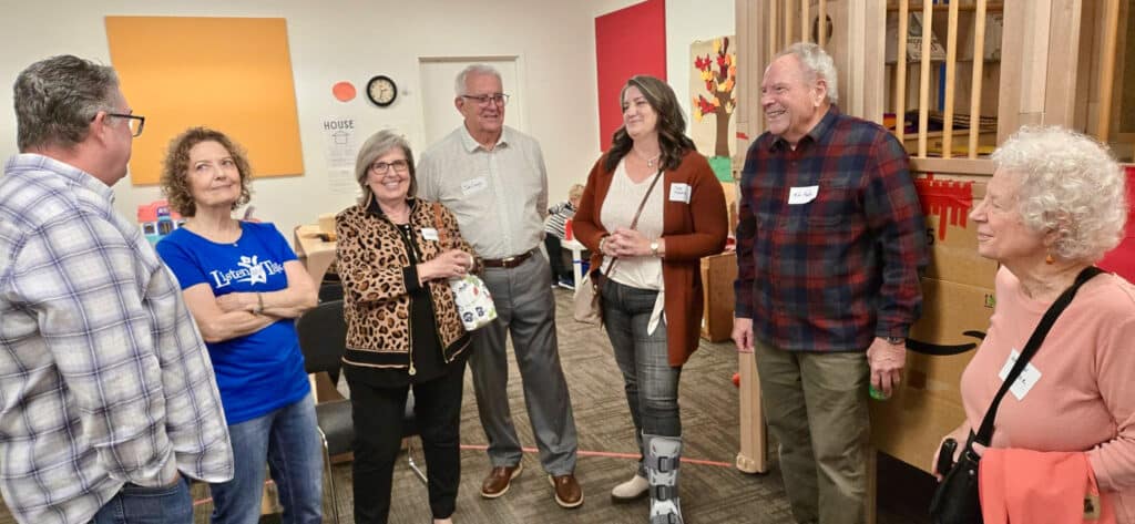 Story Time with Star Seven adults stand in a semi circle and smile as they visit with each other in a playroom with a climbing structure in the background.