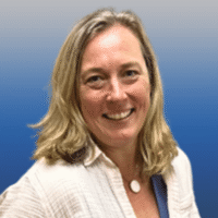 Photo of a woman with blue eyes and shoulder length blonde hair smiling. She is wearing a white collared shirt and round white necklace.